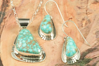 Genuine High Grade Kingman Web Turquoise set in Sterling Silver. Beautiful Pendant and Earrings Set. Created by Navajo Artist Phillip Sanchez. Signed by the artist. The Mineral Park Mine, in the Cerbat Mountains 14 miles northwest of Kingman, was first mined by Indians centuries before white man came to the area. It is one of the three sites of prehistoric mining localities in the state of Arizona. Mineral Park was the most extensively worked area by the Indians of the three. S.A. �Chuck� Colbaugh found a cache of stone hammers uncovered in ancient trenches and tunnels, when he had the turquoise mining concession in May of 1962. Ithaca Peak and Turquoise Mine (formally called Aztec Mountain or Aztec Peak) are the most famous of the peaks in the area containing turquoise.
